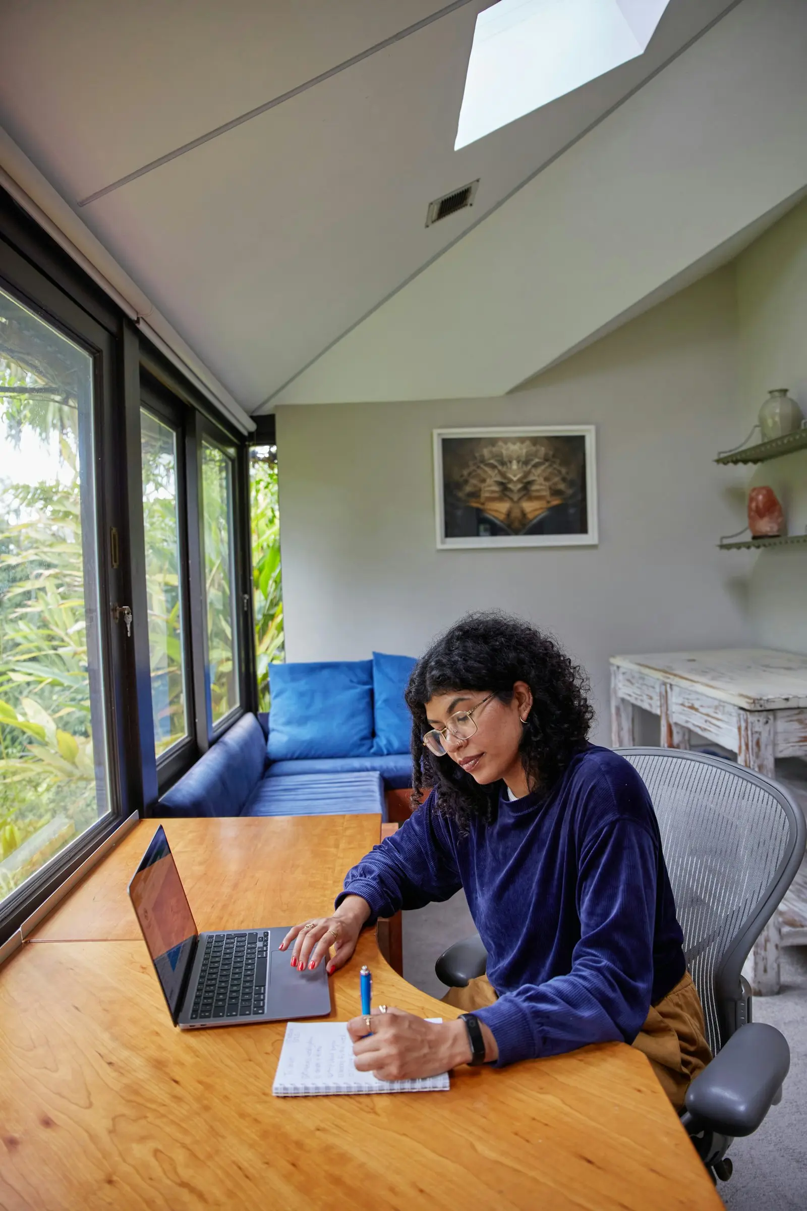 A woman working at a laptop and notebook by a window